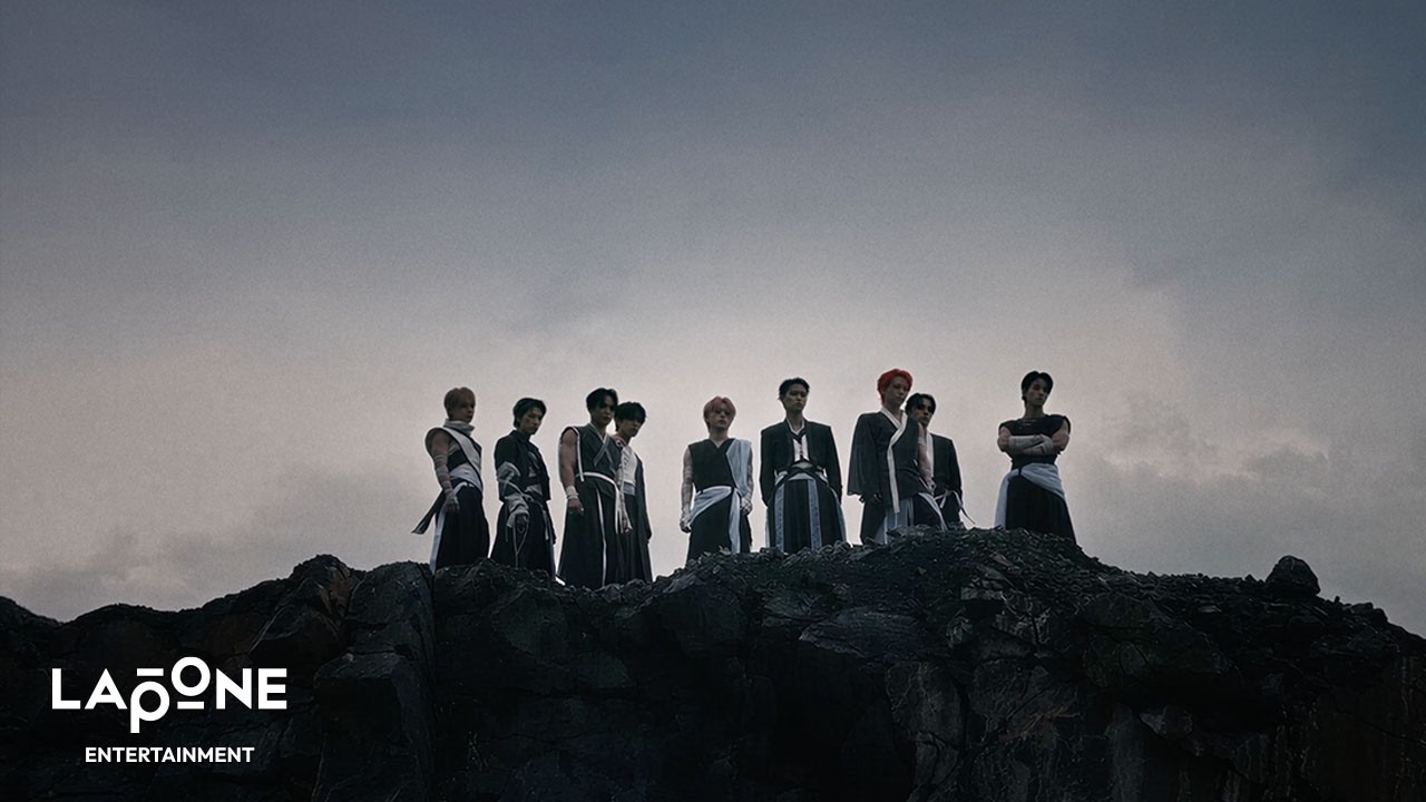 Os nove integrantes do JO1 em uma paisagem rochosa no clipe de IGNITE