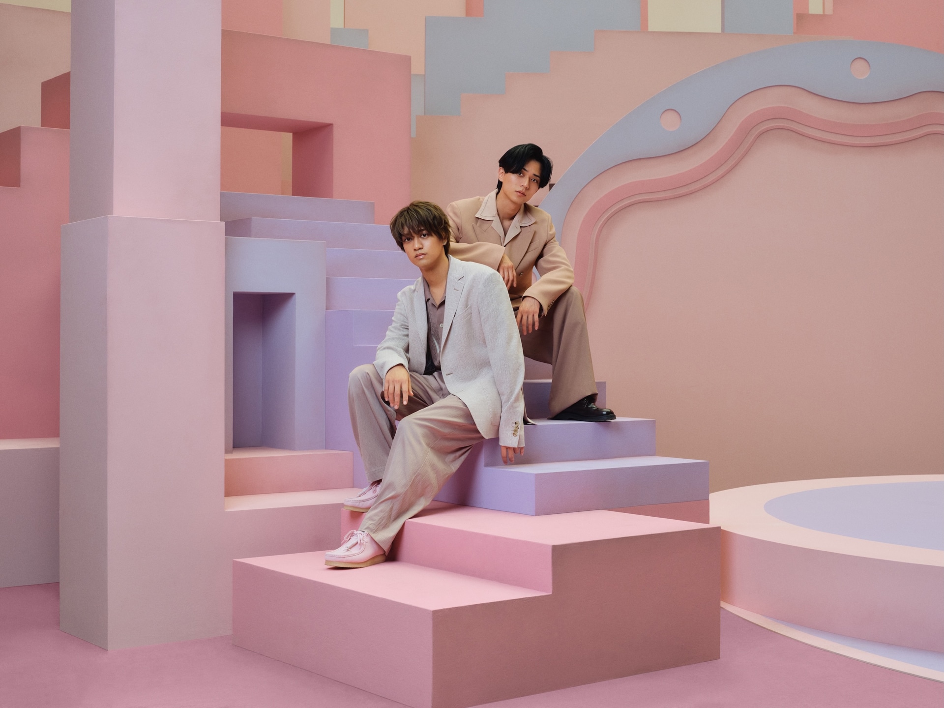 Os dois integrantes do King & Prince posam sentados em um cenário geométrico rosa e lilás