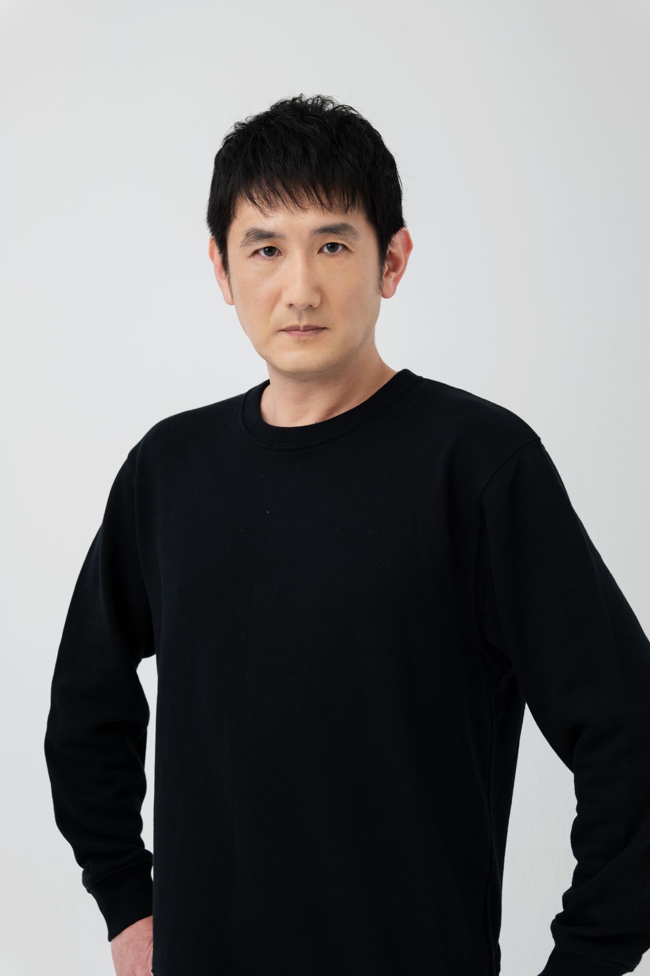 Retrato de Hiroshi Tsuchida com blusa preta diante de um fundo claro