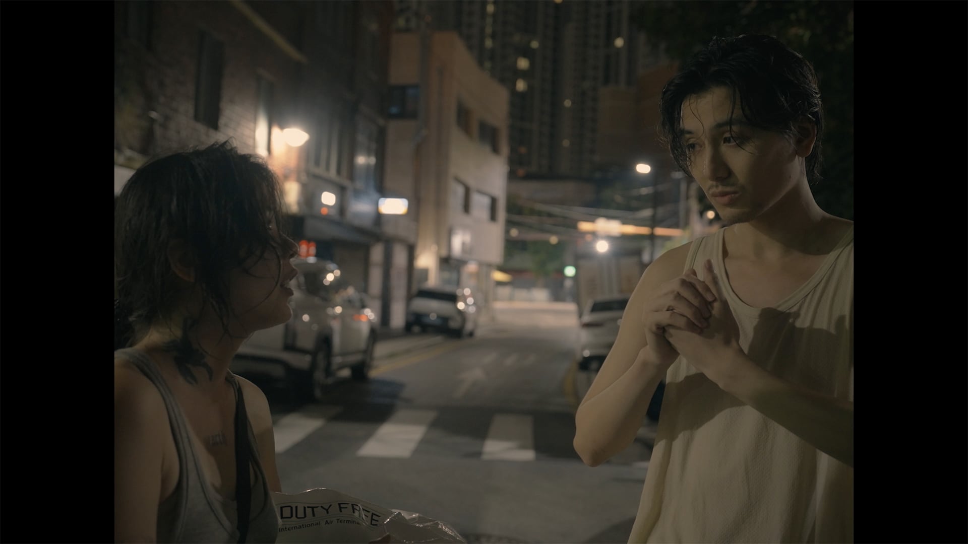 Fujii Kaze conversa com uma integrante da equipe em rua noturna na imagem do making of de You
